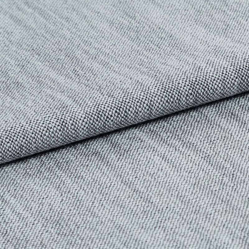 Light-gray tight basket-weave upholstery fabric, folded and layered to highlight its textured edge, photographed close-up under soft studio lighting on a neutral background.