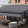 A large retractable fabric awning (dark gray, subtle diagonal stripes, front valance) mounted above sliding glass doors, extended and shading the patio; modern brick-backed outdoor seating area in daylight.