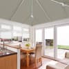 Grey pleated roof blinds with white cords, fitted across the conservatory ceiling; closed, filtering daylight over a bright kitchen-dining area with white-framed doors and windows opening to a patio garden.