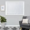 White vertical blinds covering a window, narrow fabric slats with scalloped bottoms; closed and diffusing soft daylight; living-room setting with grey armchair, knitted throw, potted plant, framed art.