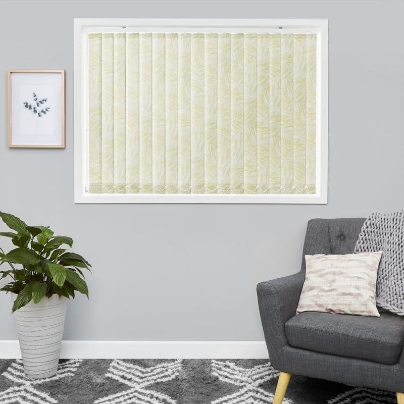 Pale green leaf-patterned vertical blinds, closed and diffusing light over a white-framed window; gray living room with armchair, knitted throw, potted plant and botanical wall art.