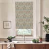 Patterned floral-and-bird roller blind covers a kitchen window, hanging down above a stainless faucet and sink; marble countertop, wooden cabinets, potted plants and framed sketch flank the window.