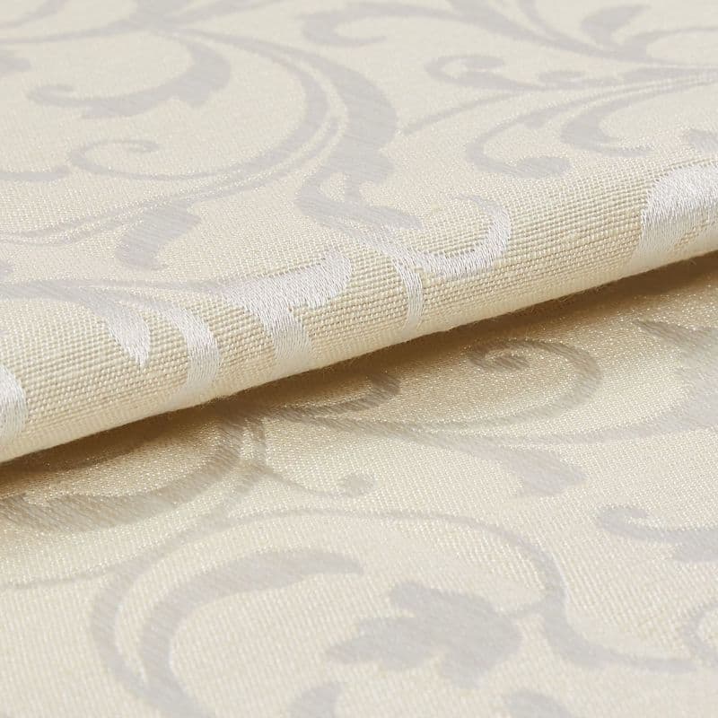 Cream damask curtain fabric swatch, folded with raised woven scroll motifs, reflecting subtle sheen; close-up macro view showing textured weave and soft studio lighting on a neutral surface.