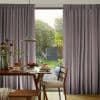 Floor-length pleated patterned curtains, pulled to sides with a central opening, framing a glass door; filtering daylight into a dining area with wooden table set for breakfast and garden beyond.