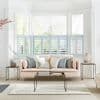 Pale-blue café-style plantation shutters cover the lower halves of a bay window; slatted panels partially open, filtering daylight into a bright living room with pastel sofa, cushions and coffee table.