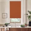 Rust-colored roller blind covers most of a kitchen window above a stainless sink; marble countertop holds a towel, bowl of greens, potted plants, and a framed sketch on a pale wall.