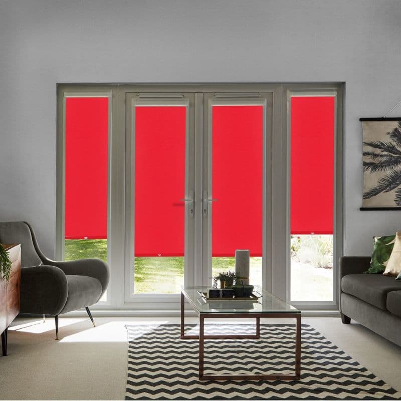 Four red roller blinds covering tall French doors and sidelights, lowered to mid-height, blocking light; modern living room with grey armchairs, glass coffee table, chevron rug, daylight and garden beyond.