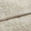 Folded beige velvet-look curtain fabric, horizontally creased and showing irregular brushed texture; displayed flat under soft, neutral studio lighting suggesting a fabric sample rather than a furnished room.