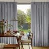 Floor-length grey pleated curtains, parted centrally, framing a glass door; filtering daylight into a dining nook with wooden table, pendant lamp, pancakes on plates, chairs, and a leafy garden view.