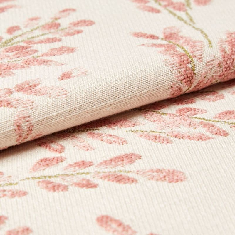 Cream woven fabric with raised pink floral embroidery, folded over along a seam; tufted stitches form leaf clusters. Close-up view of textured textile under soft, neutral lighting.