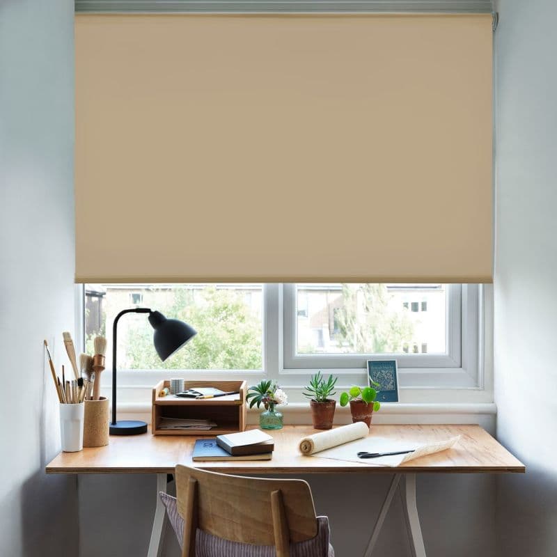 Beige roller blind, mounted at the top and lowered to just above the sill, filtering daylight; wooden desk beneath with lamp, art brushes, small potted succulents and workspace supplies.
British Herbs