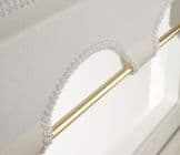 White scalloped‑trim fabric blind looped over a polished brass rod, crocheted edging forming decorative arches; partially raised, filtering soft daylight above white window frame in a bright room.
