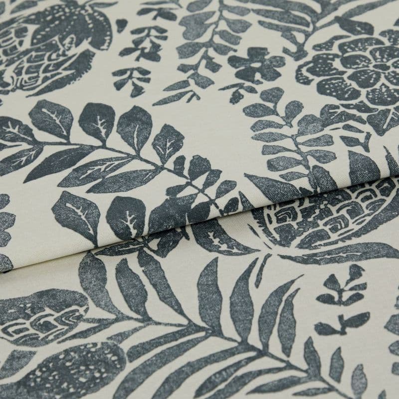 A folded cream textile with dark blue-gray botanical block-print; fabric overlapping to reveal repeated leaves and flowers; close-up studio view with soft, even lighting highlighting weave texture.