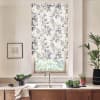 Patterned roller blind covers window, filtering light; over kitchen sink with chrome faucet on marble countertop, wooden cabinets below, with potted plants, bowl of greens and framed sketch.