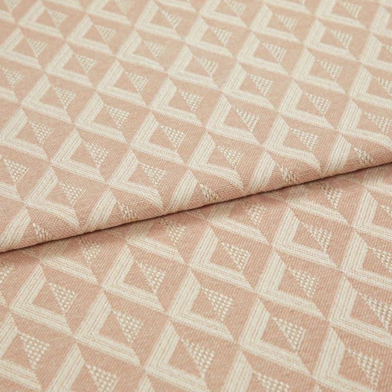 Woven pink geometric jacquard fabric, folded over itself, displaying raised cream triangular diamond pattern; close-up on a flat surface with soft, even studio lighting emphasizing texture.