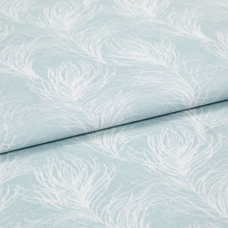 Light blue cotton fabric featuring white peacock-feather motifs, folded once so layers overlap; printed pattern repeats across a soft textile surface in bright, even studio lighting, close-up view.