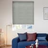 Pleated grey cellular blind, lowered to just above the sill with horizontal ribs, blocking most light; living room with blue sofa, cushions, floor lamp, framed art, roof and trees outside.