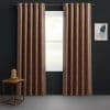 Grommet-top patterned curtains with orange-brown lattice, hung on a metal rod, partially open and filtering daylight through the window; dark-walled room with wooden side table and framed abstract art.