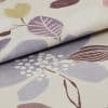 Folded woven fabric sample with pastel leaf-and-dot print — layered and overlapping, revealing textured weave — close-up macro on a neutral surface, softly lit to emphasize pattern and folds.