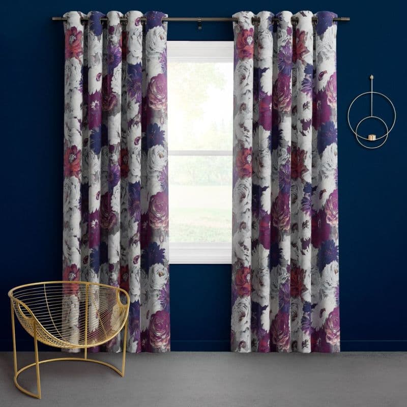 Grommet-top floral curtains (white with purple and magenta blooms) hang on a metal rod, drawn slightly apart and filtering daylight through a centered window; navy-painted wall, gold wire chair nearby.