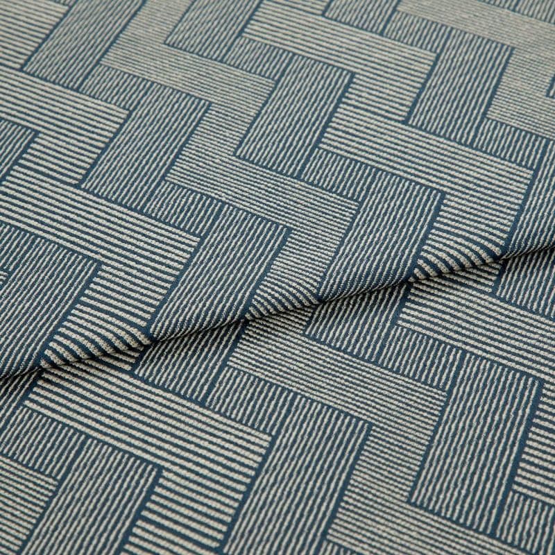 Blue-and-cream woven fabric with interlocking rectangular striped pattern, partially folded and layered, showing raised texture and seam — close-up on a flat surface under soft studio lighting.