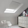 Room with white eaves wall, dark blue-grey wall to right with a shabby chic white drawer unit, a contemporary white chair, white painted floorboards and a skylight blind in pale flint grey.