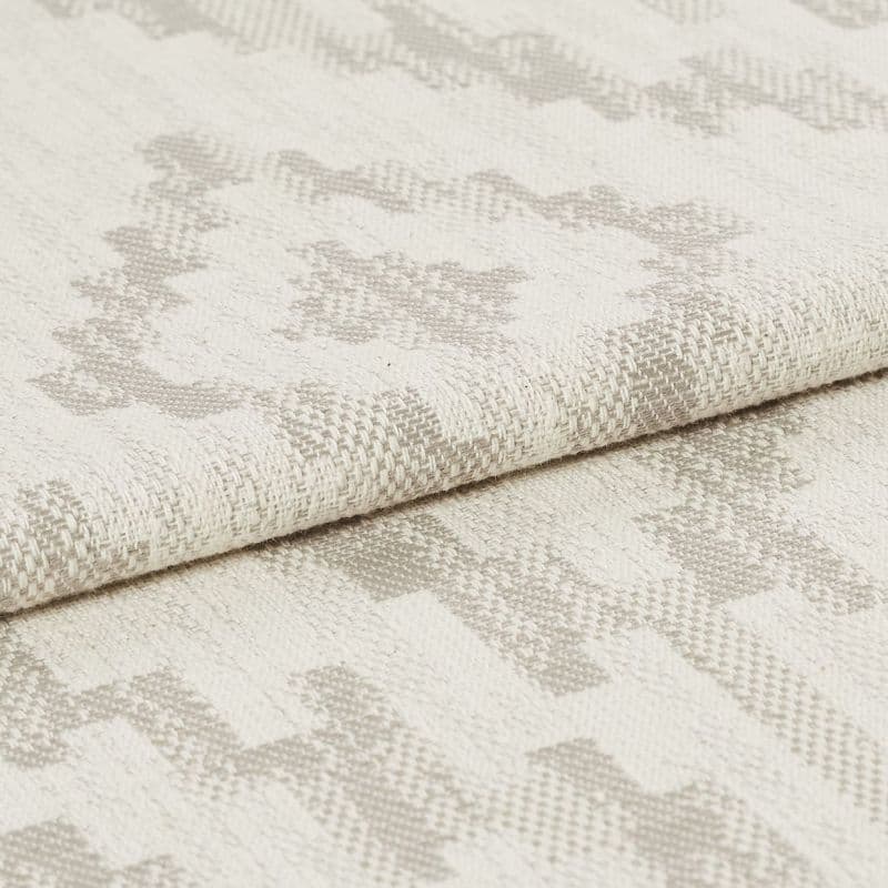 Woven upholstery fabric with light beige geometric motif, folded over once showing textured weave; close-up studio shot with neutral lighting emphasizing fibers and subtle pattern.