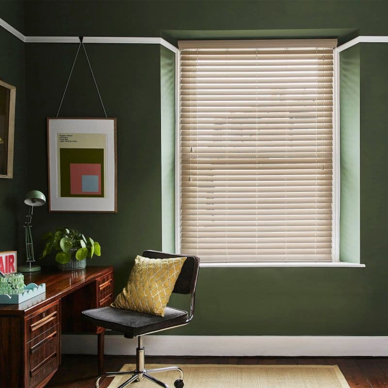 Beige horizontal venetian blinds mounted inside a window recess, slats mostly closed, filtering soft daylight; small dark-green home study with wooden desk, swivel chair and yellow cushion.
AIR